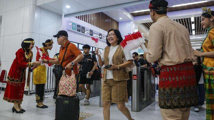 Petugas berpakaian adat daerah memberikan pin dan bendera kepada penumpang di Stasiun Kereta Cepat Whoosh Halim, Jakarta